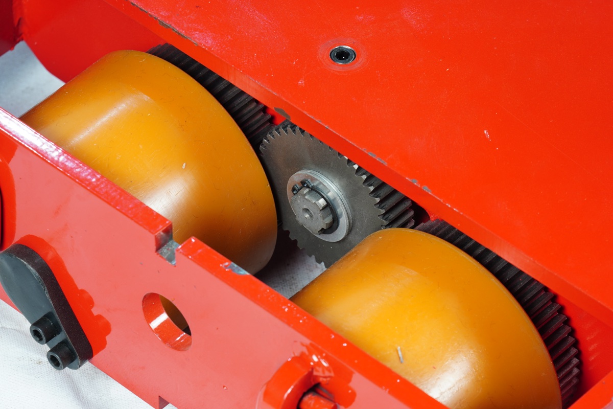 Internal drive mechanism — two large orange polyurethane drive wheels meshed with steel pinion gear inside red chassis frame